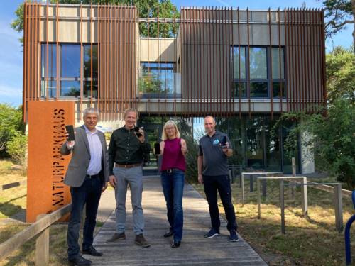 Vier Menschen mit Smartphones in den Händen vor einem architektonisch interessanten Gebäude, dem Naturparkhaus in Mardorf